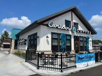 Caribou Coffee building with white board-and-batten siding, a stone base and a fenced patio