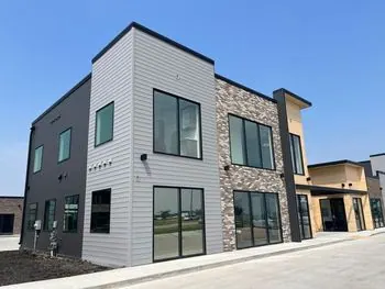 Two-story commercial building with gray lap siding, dark panels and stone veneer
