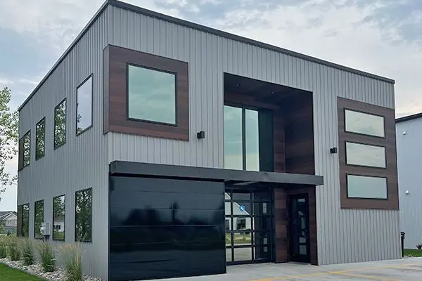 Corner view of a modern commercial building with gray metal siding and a black glass garage door