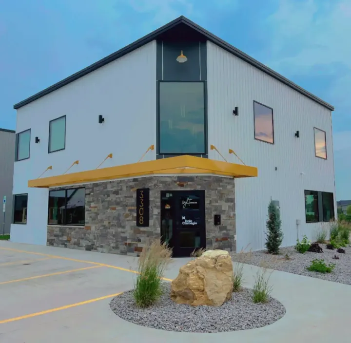 Two-story commercial building with light gray siding, stone base and yellow entry awning